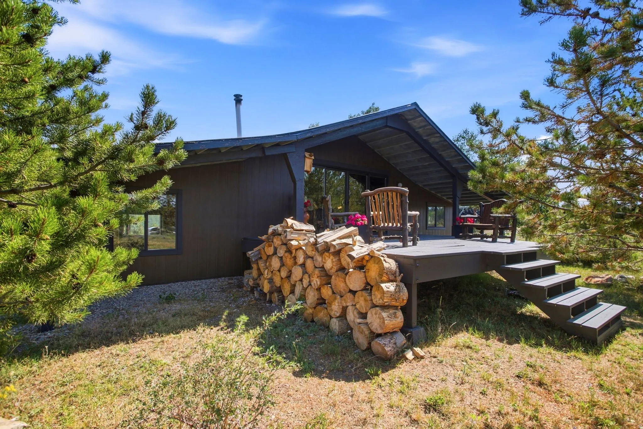 Exterior featuring a covered deck, wood siding, a metal chimney, and surrounding mature trees