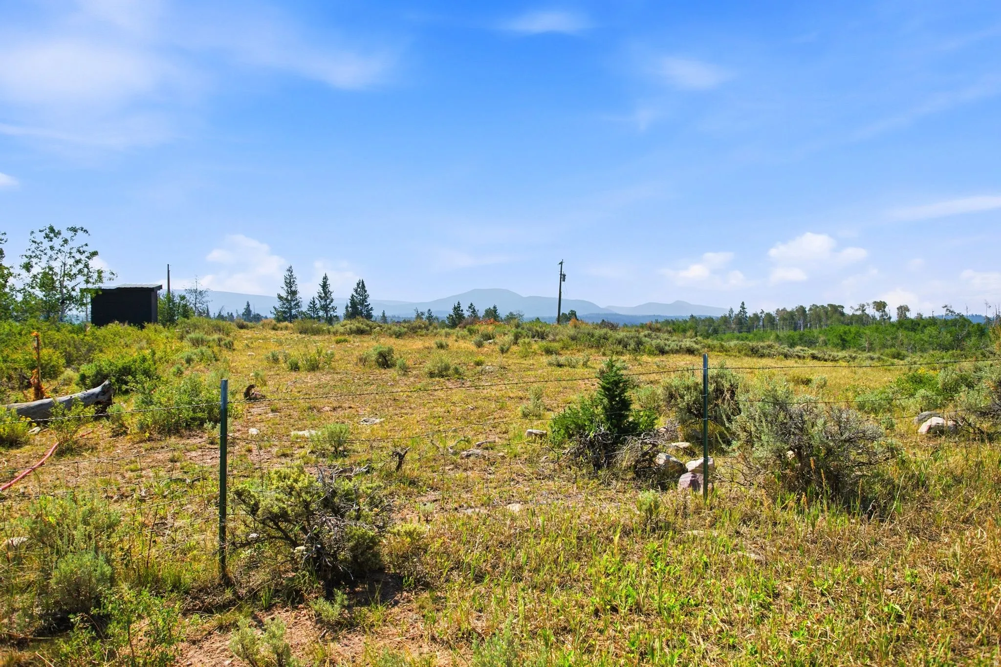Expansive lot with distant mountain ranges, scattered trees, and a clear blue sky
