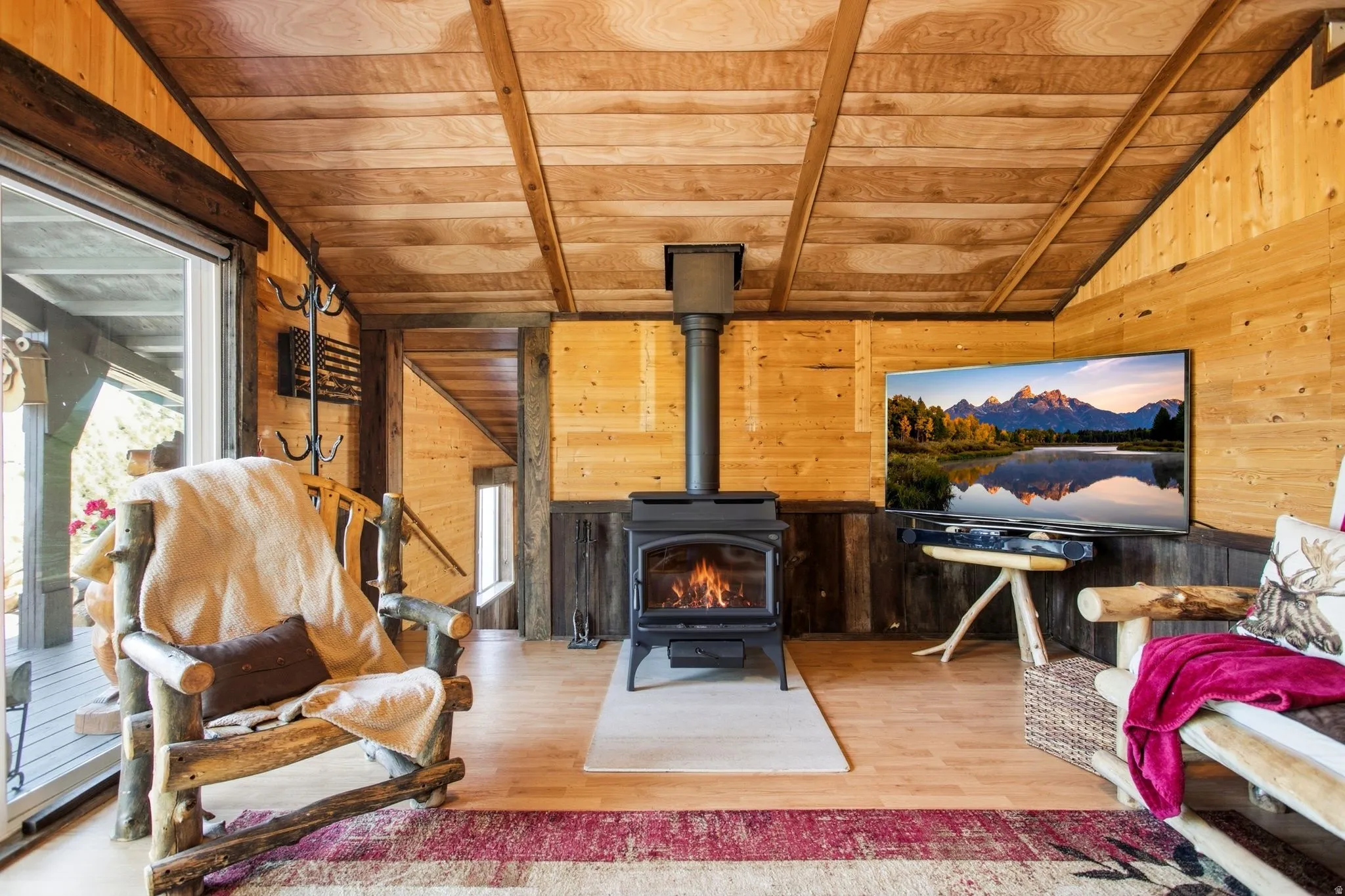 Vaulted wood-paneled ceiling, wood-finish wall paneling, wood-finish flooring, black wood-burning stove, and glass sliding door