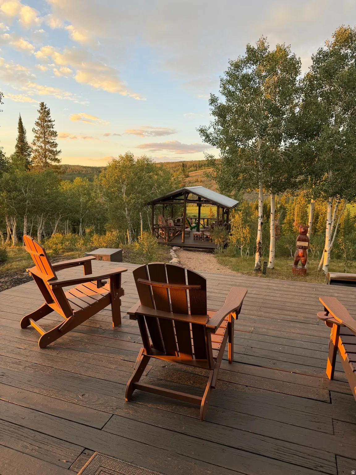 Expansive outdoor deck featuring composite decking and a built-in wooden gazebo with a metal roof, surrounded by mature trees and natural landscaping