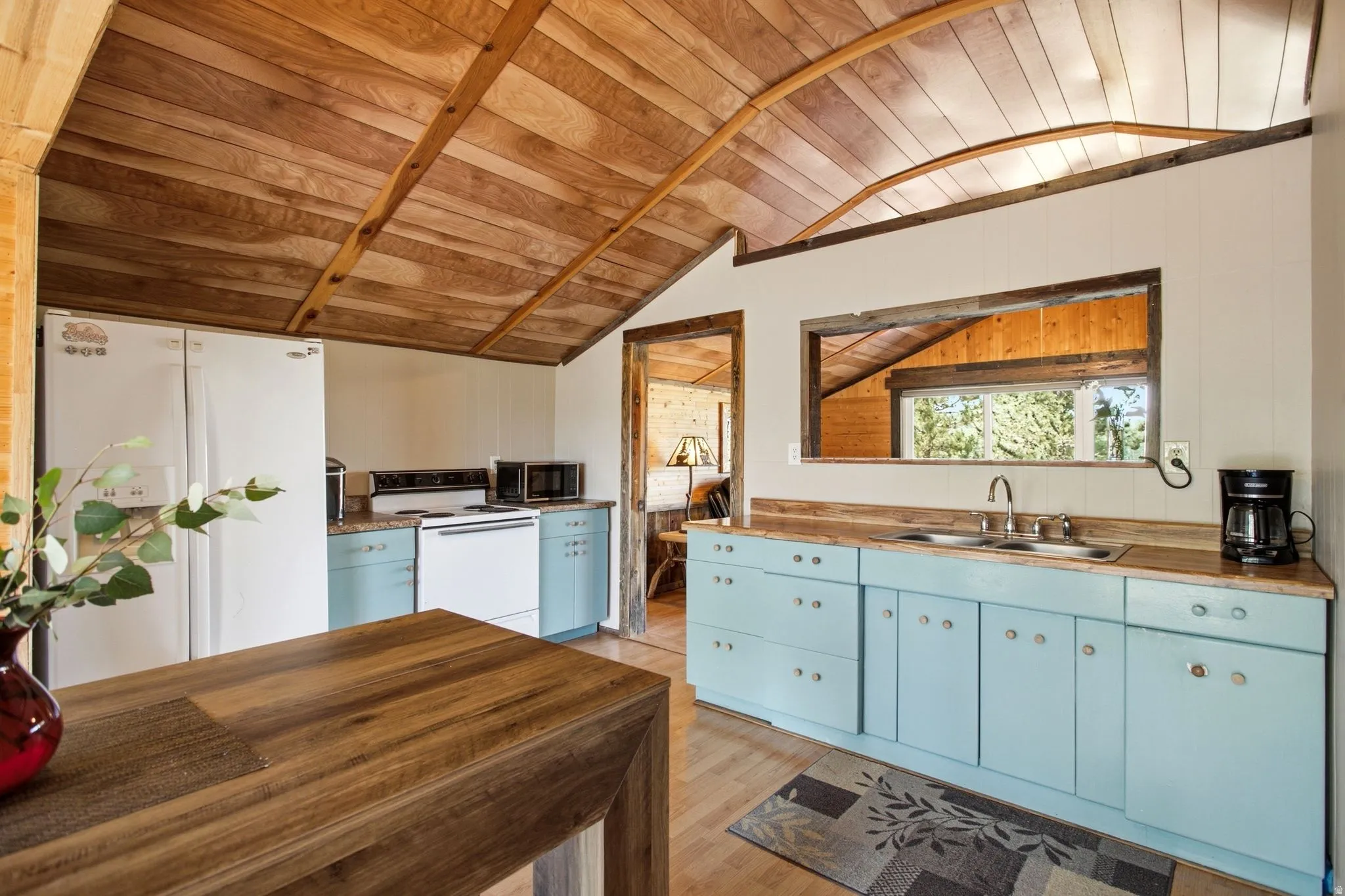 Angled wood-finish plank ceiling, light blue base cabinetry, wood-finish countertops, and a double basin stainless steel sink