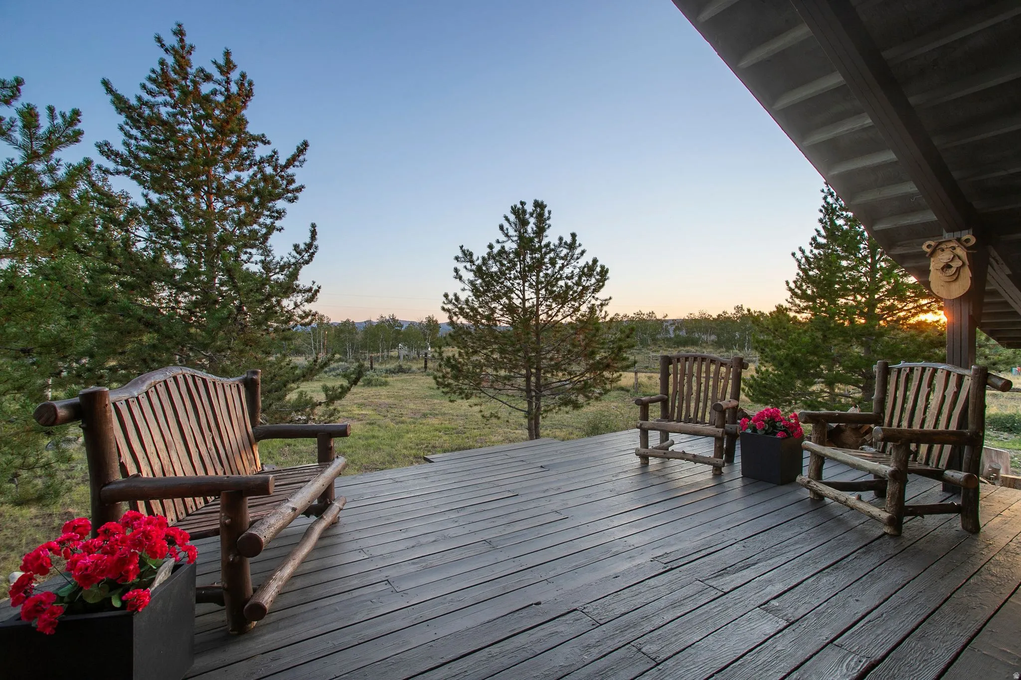 Expansive outdoor deck with wood flooring, featuring a rustic wood bench and two matching chairs