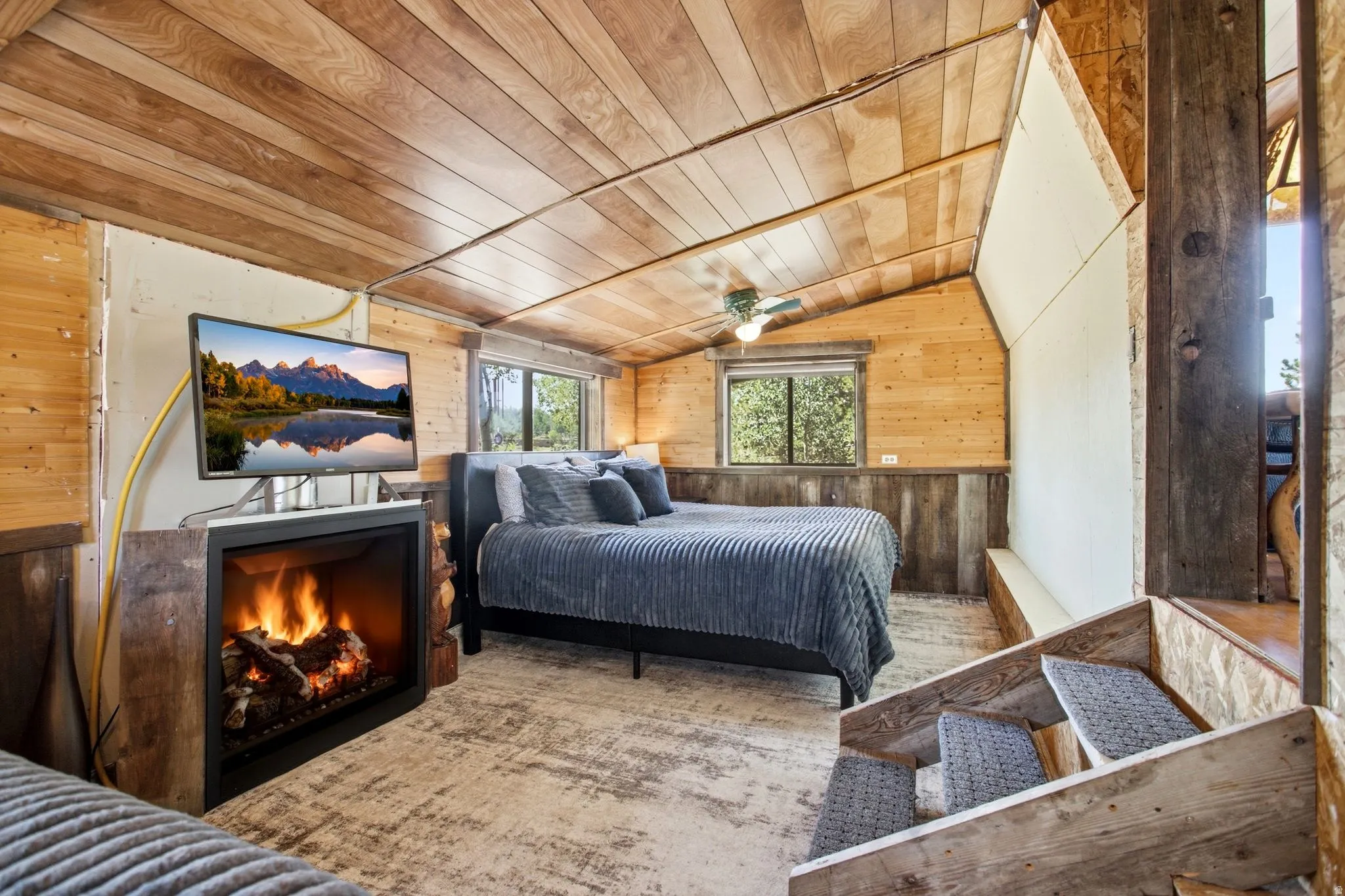 Wood-paneled walls and ceiling with an angled roofline, featuring an electric fireplace and ceiling fan
