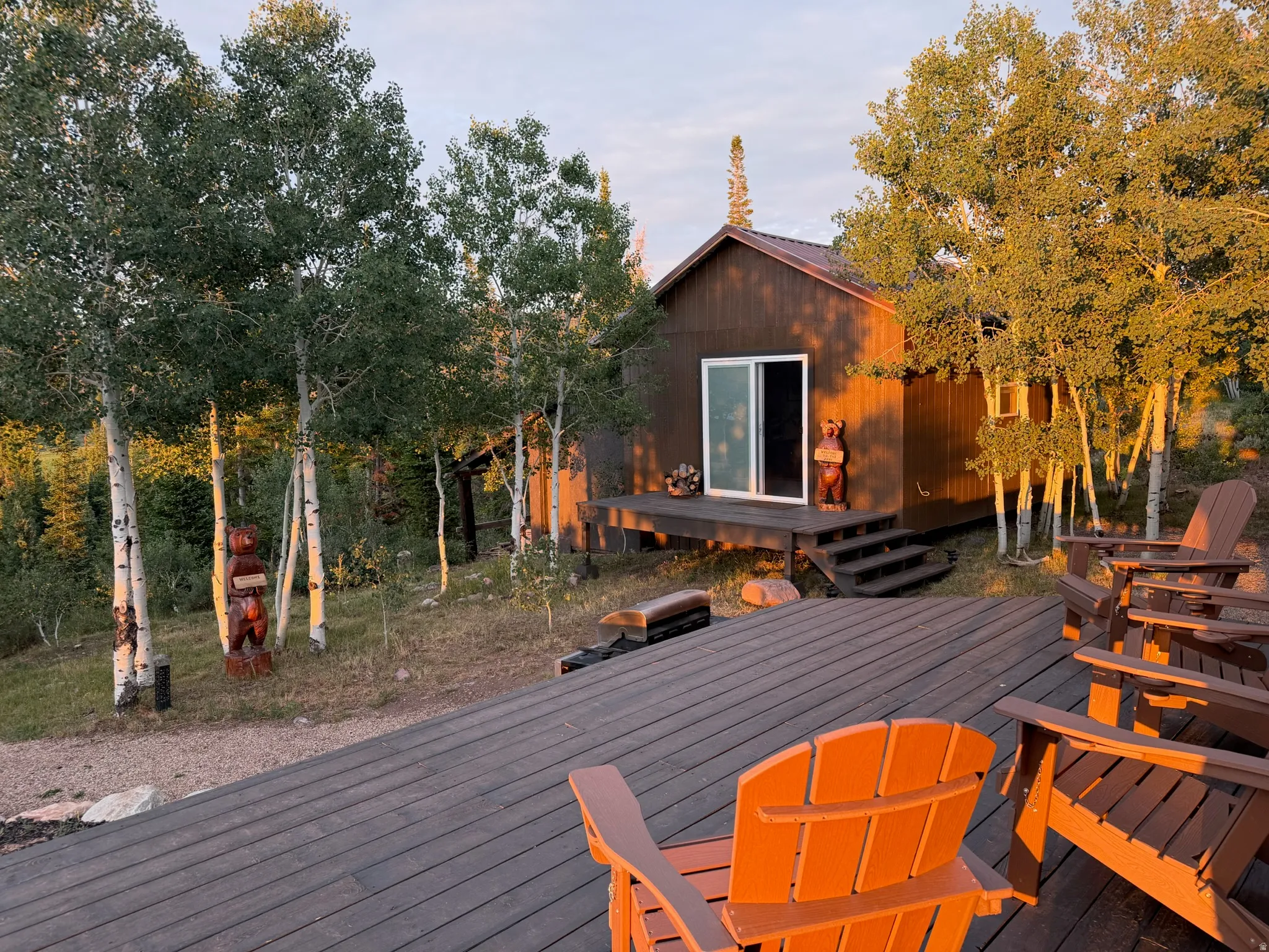 Exterior featuring a spacious wood-finish deck, sliding glass door, and surrounding mature trees