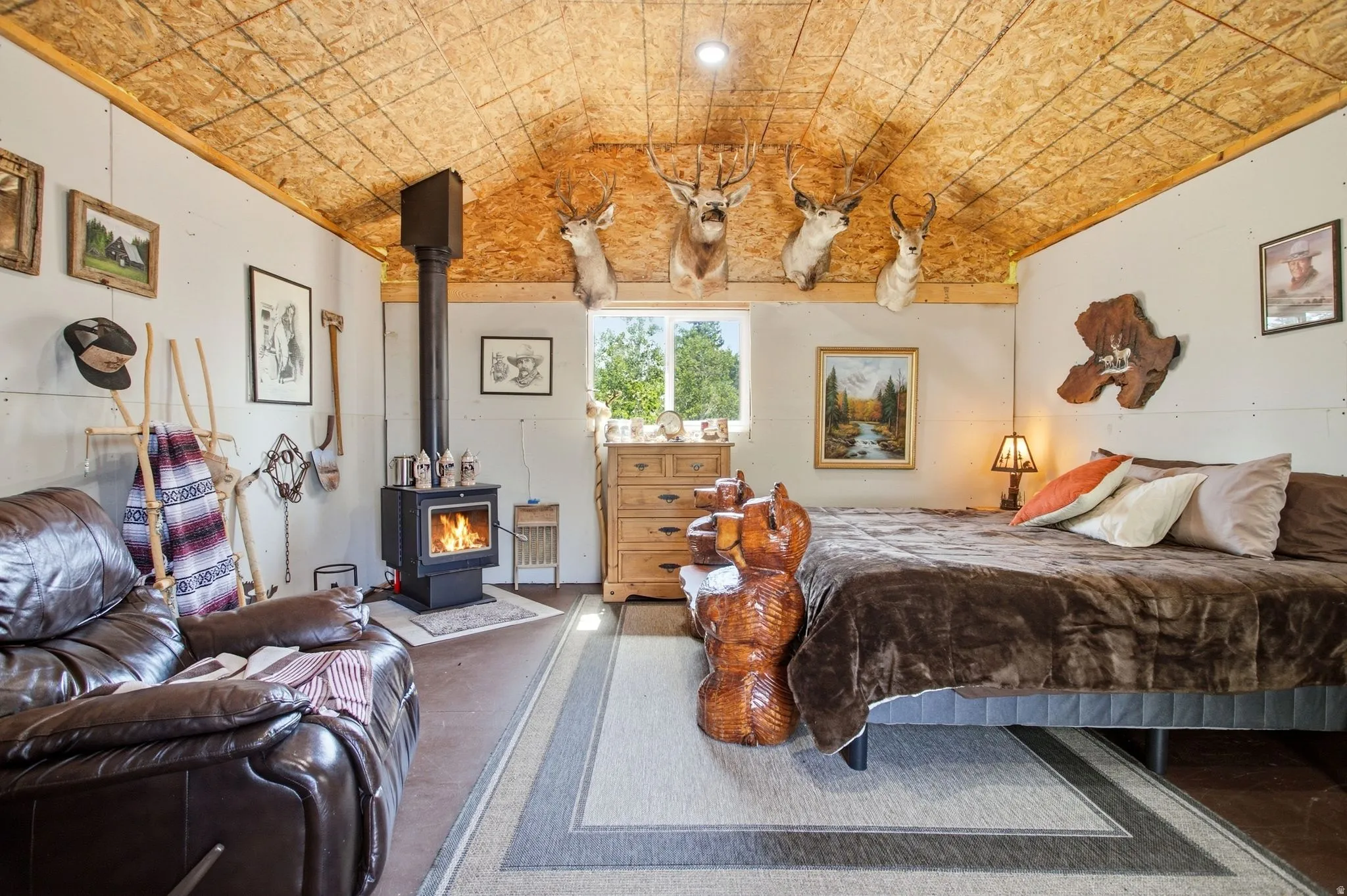 Bunkhouse with sloping wood-finish ceiling, wood-burning stove with metal flue, exposed wall framing, and a natural wood-finish dresser
