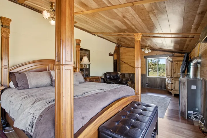 Vaulted wood-paneled ceiling, wood-finish flooring, accent wood paneling, wood window trim, and a ceiling fan with integrated lighting