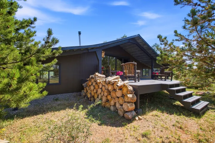 Exterior featuring a covered deck, wood siding, a metal chimney, and surrounding mature trees