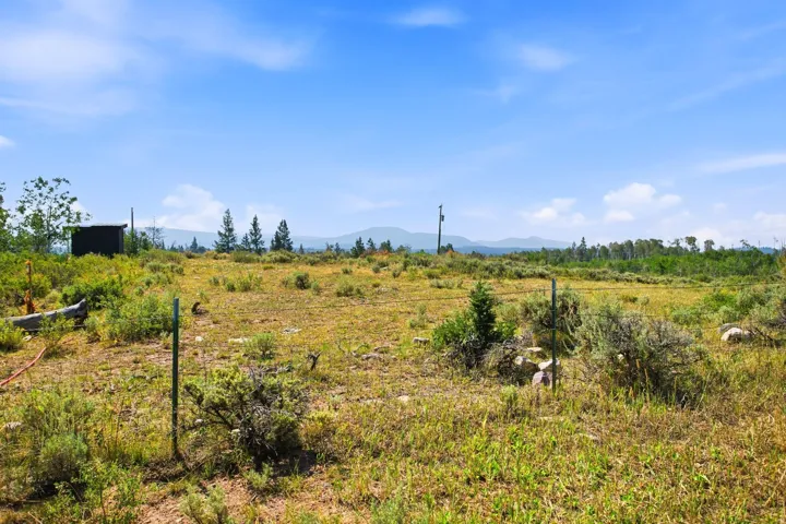 Expansive lot with distant mountain ranges, scattered trees, and a clear blue sky