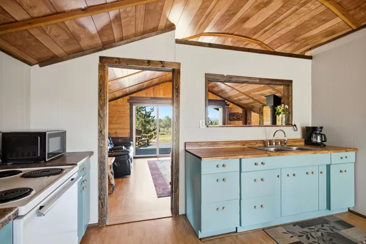 Wood-finish vaulted ceiling, wood-finish flooring, wood-finish countertops, light blue base cabinetry, and a stainless steel sink