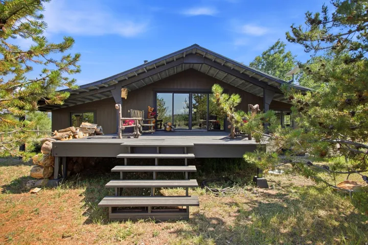 Exterior featuring a gabled roofline, dark horizontal siding, expansive deck, and large sliding glass doors