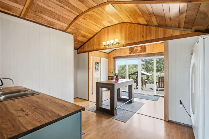 Vaulted wood-paneled ceiling, wood-finish flooring, wood countertops with double basin sink, white paneled walls, and sliding glass doors to outdoor deck