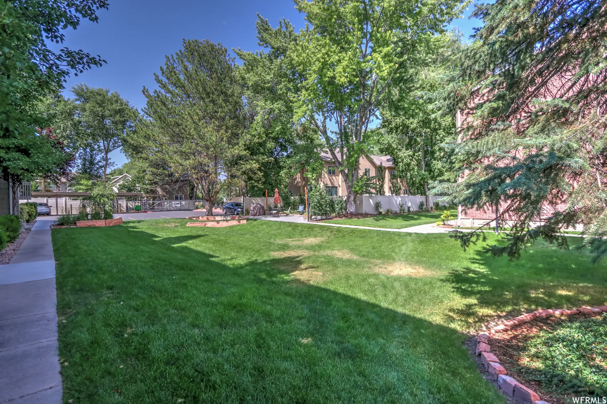 Expansive green space featuring a manicured lawn, mature trees, and a paved walkway