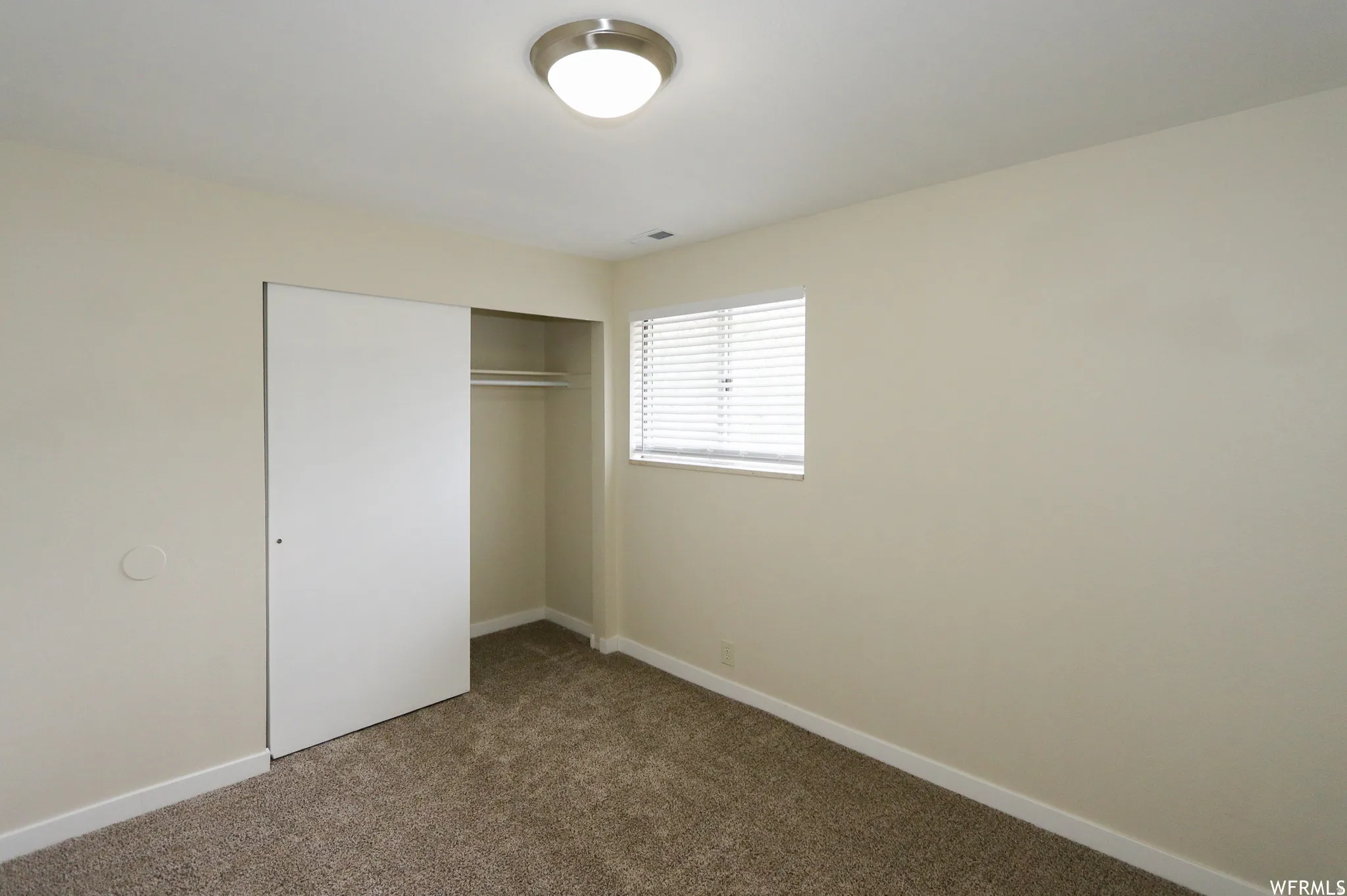 Neutral wall paint, window with horizontal blinds, flush mount ceiling light, sliding closet door, and carpeted flooring