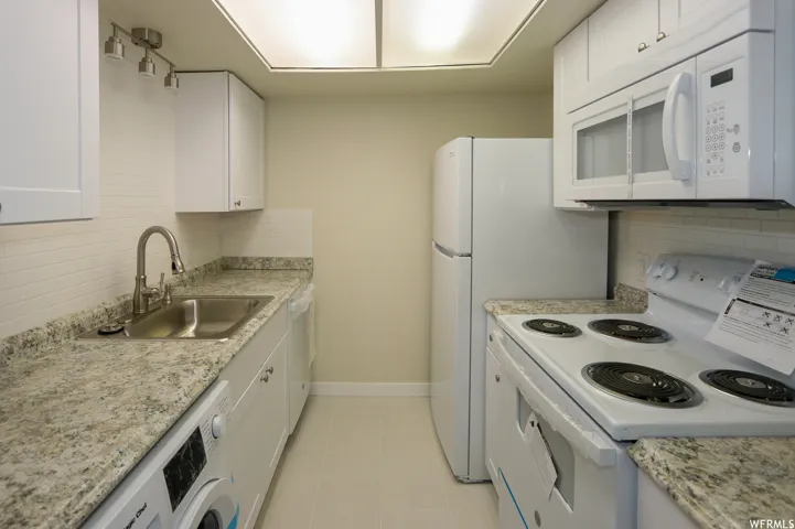 Galley kitchen featuring white cabinetry, light-toned countertops, tile flooring, and integrated white appliances