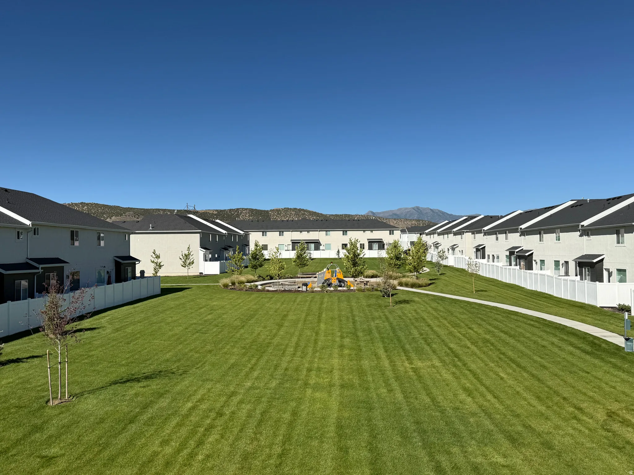 Expansive common green space featuring a manicured lawn, paved walking path, and a playground area