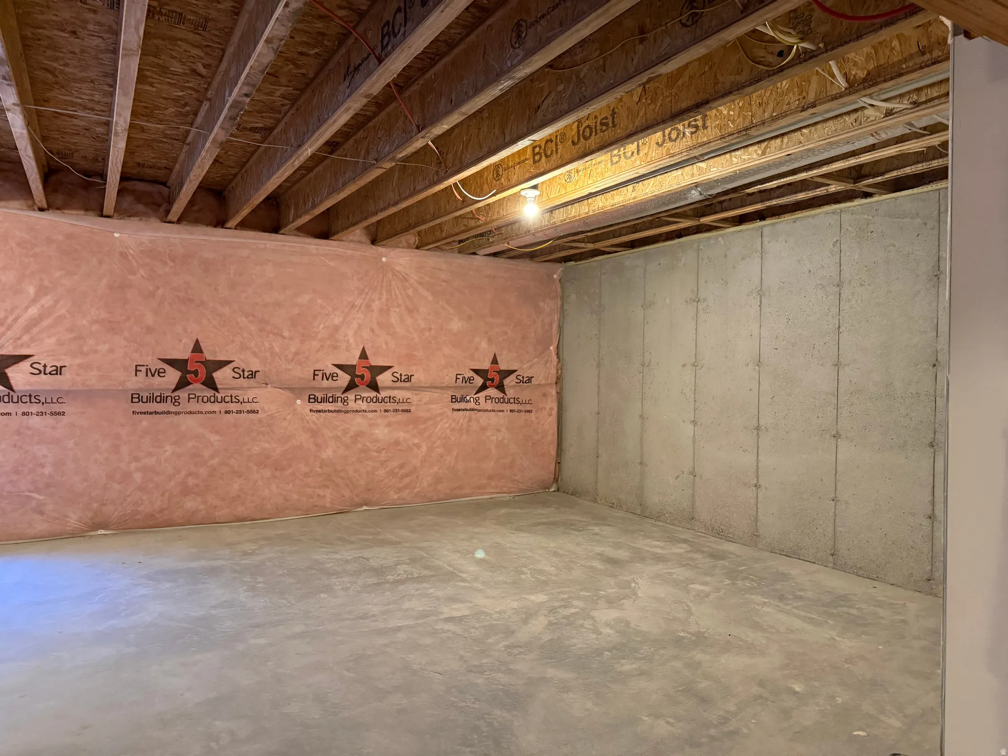 Unfinished basement featuring exposed wood joists, concrete walls, and insulated wall sections