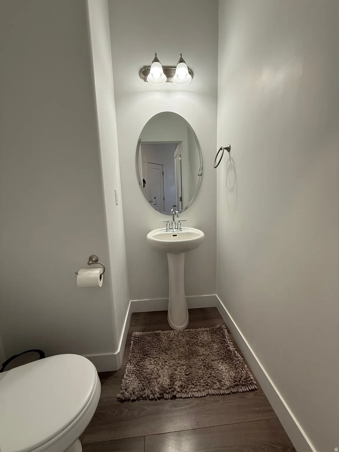 Pedestal sink with chrome faucet, oval mirror, and wood-finish flooring