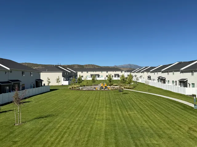 Expansive common green space featuring a manicured lawn, paved walking path, and a playground area
