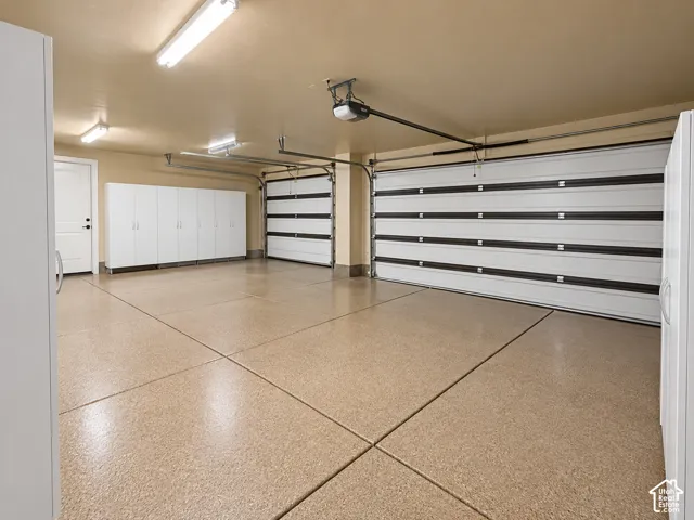Spacious three-car garage featuring an epoxy-coated concrete floor. AI alteration to remove all belongings of owners. White built in cabinets for storage.