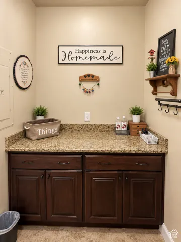 Granite-look countertop, rich wood-finish cabinetry, under-cabinet storage, and built-in wall shelf