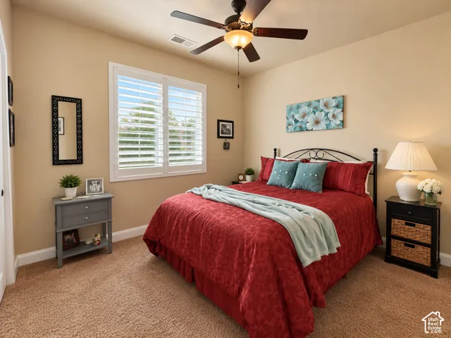 Carpeted bedroom featuring a ceiling fan with integrated lighting, a window with plantation shutters, and light-toned walls