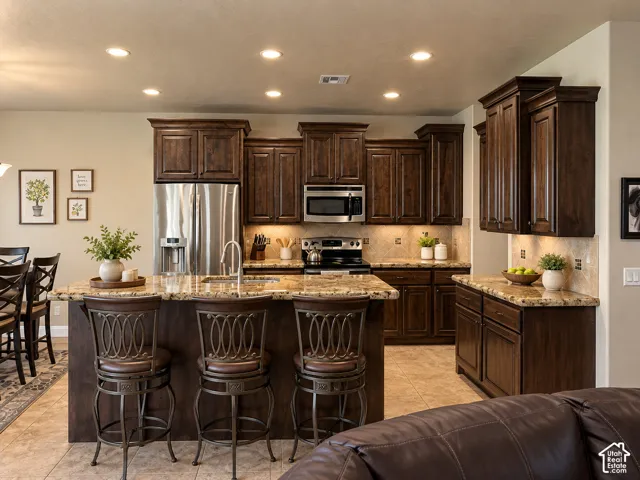 Kitchen featuring dark wood cabinetry, granite countertops, stainless steel appliances, a tiled backsplash, and recessed lighting