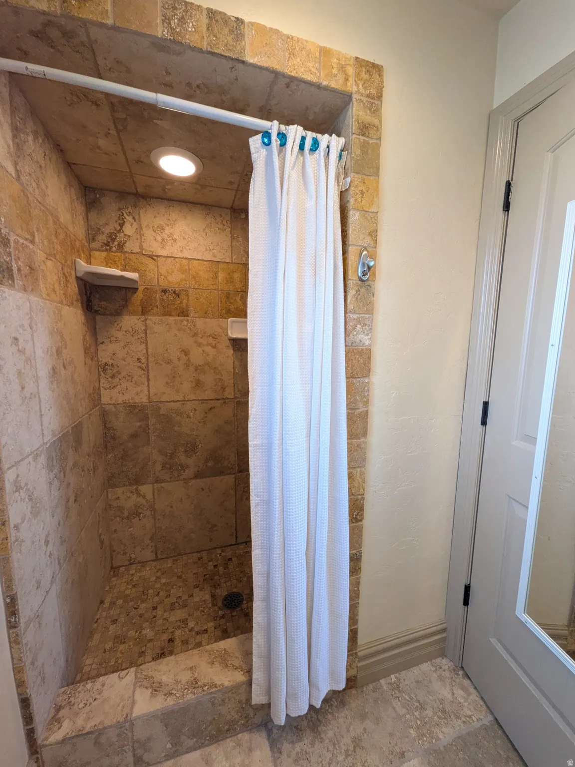 Tiled shower enclosure with built-in shelving, recessed lighting, and a mosaic tile floor