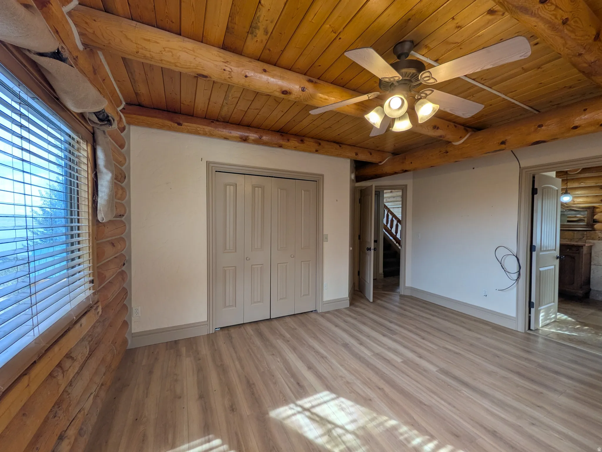 Wood-finish flooring with a ceiling fan light fixture, double bi-fold closet doors, and exposed wood beams