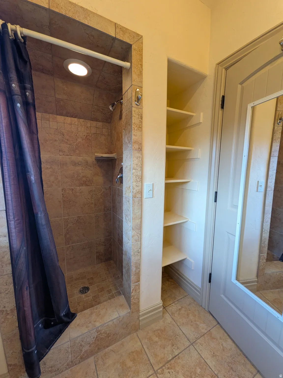 Tiled shower with a recessed ceiling light, built-in shelving, and tiled flooring