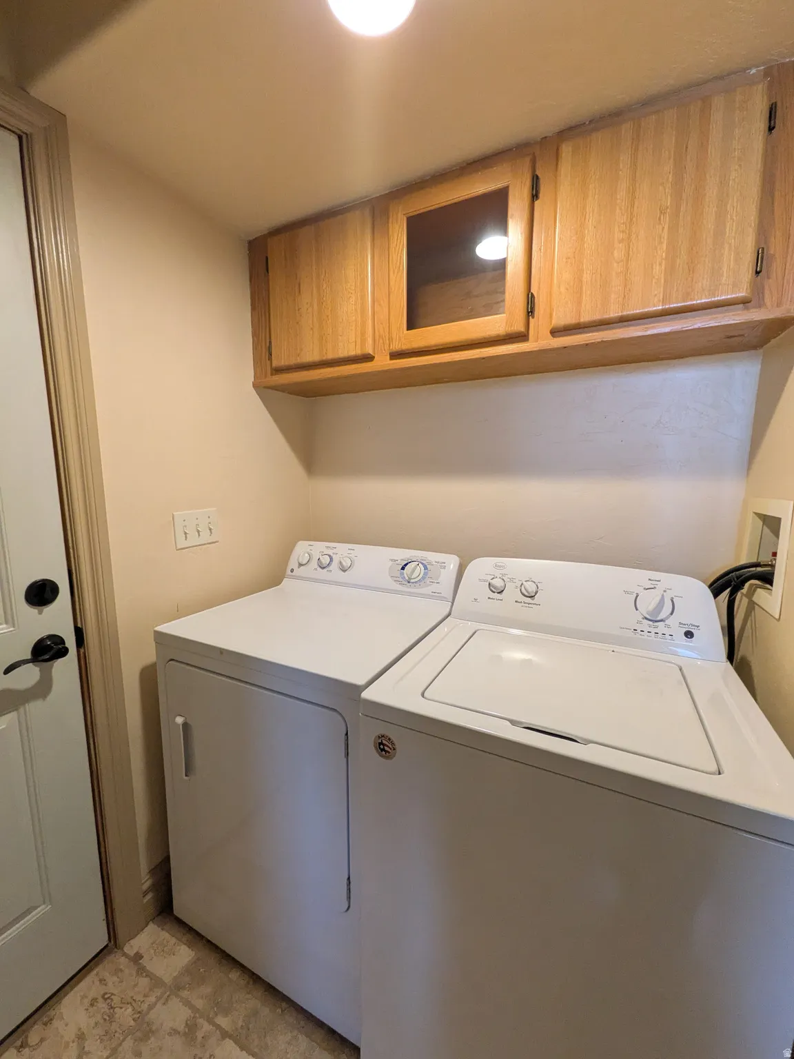 Utility area featuring built-in wood cabinetry with glass-front accents and overhead lighting