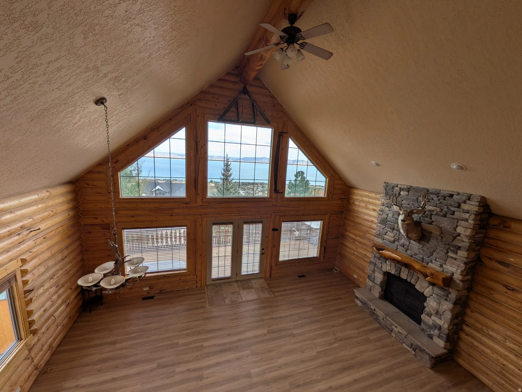 Vaulted ceiling with exposed wood-finish beams, large windows, stone fireplace, wood-finish flooring, and log wall construction