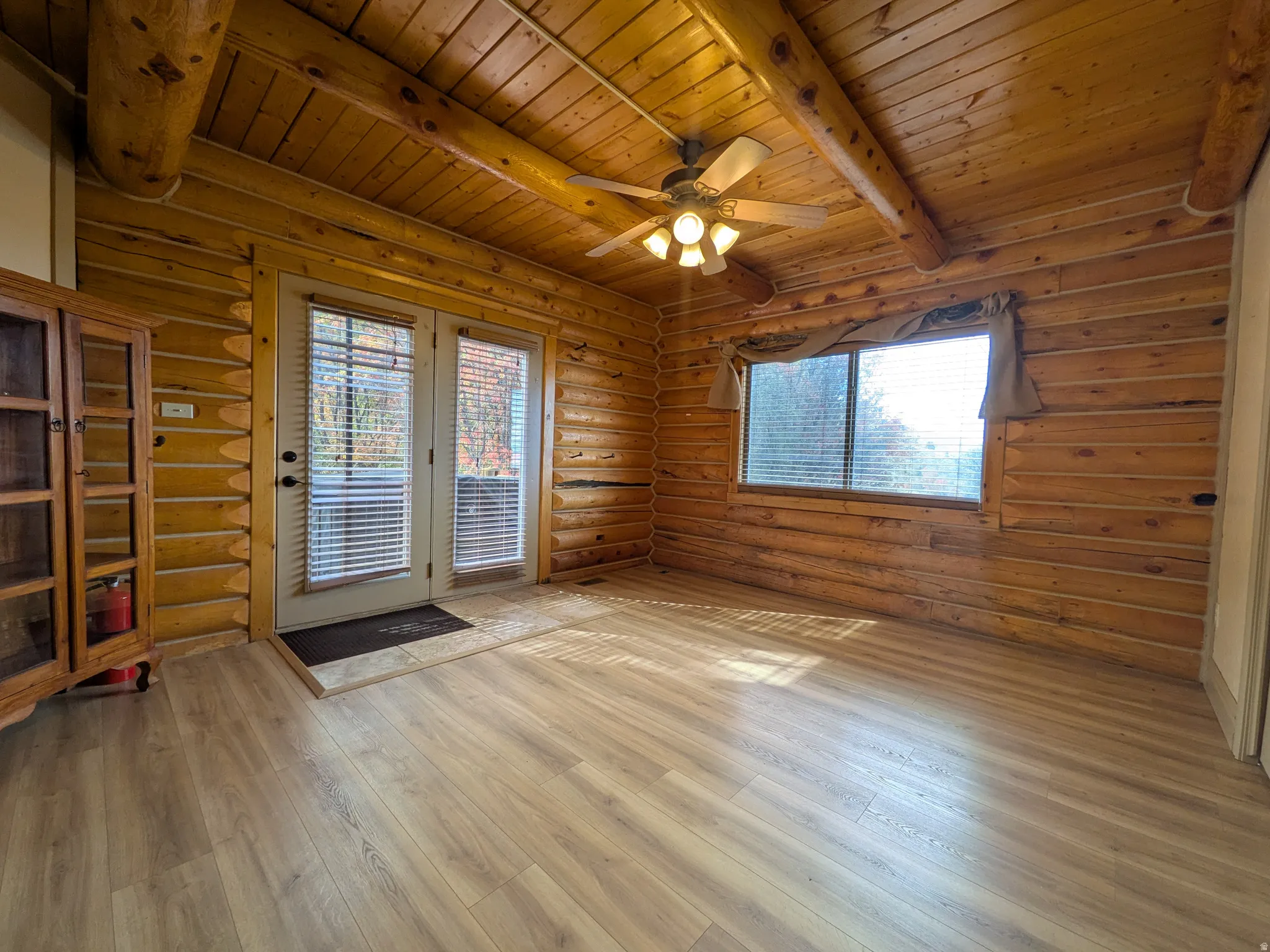 Wood-finish flooring, exposed wood beam ceiling, wood plank walls, ceiling fan with integrated lighting, and a double-door exterior entry