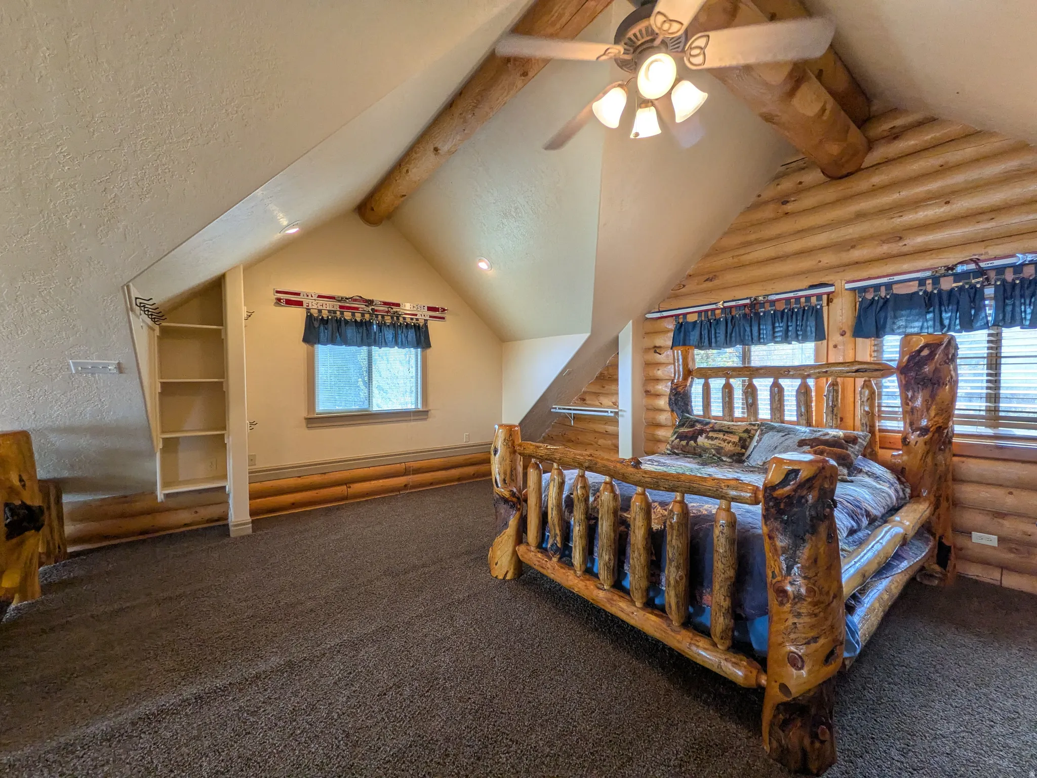 Sloped ceilings featuring wood beams, built-in shelving, carpet flooring, and log-style wall finishes