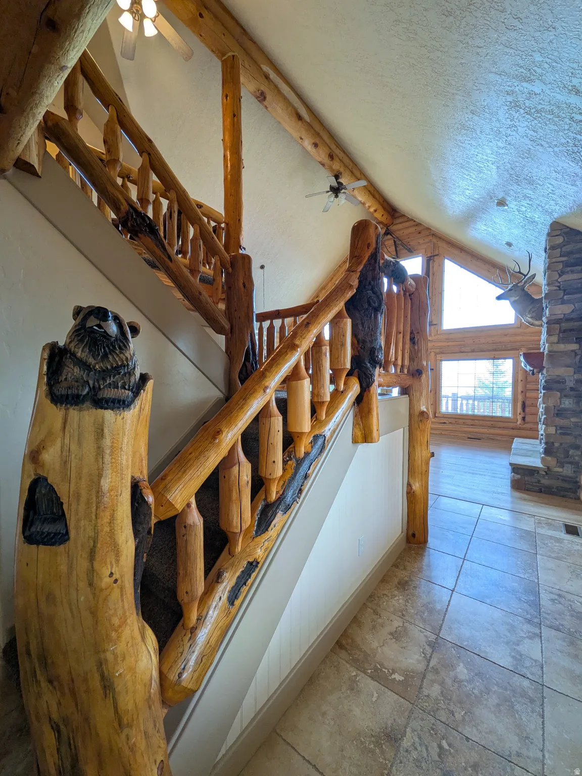 Rustic wood staircase with custom carved newel post, tile flooring, wood-beamed ceilings, and a stone fireplace