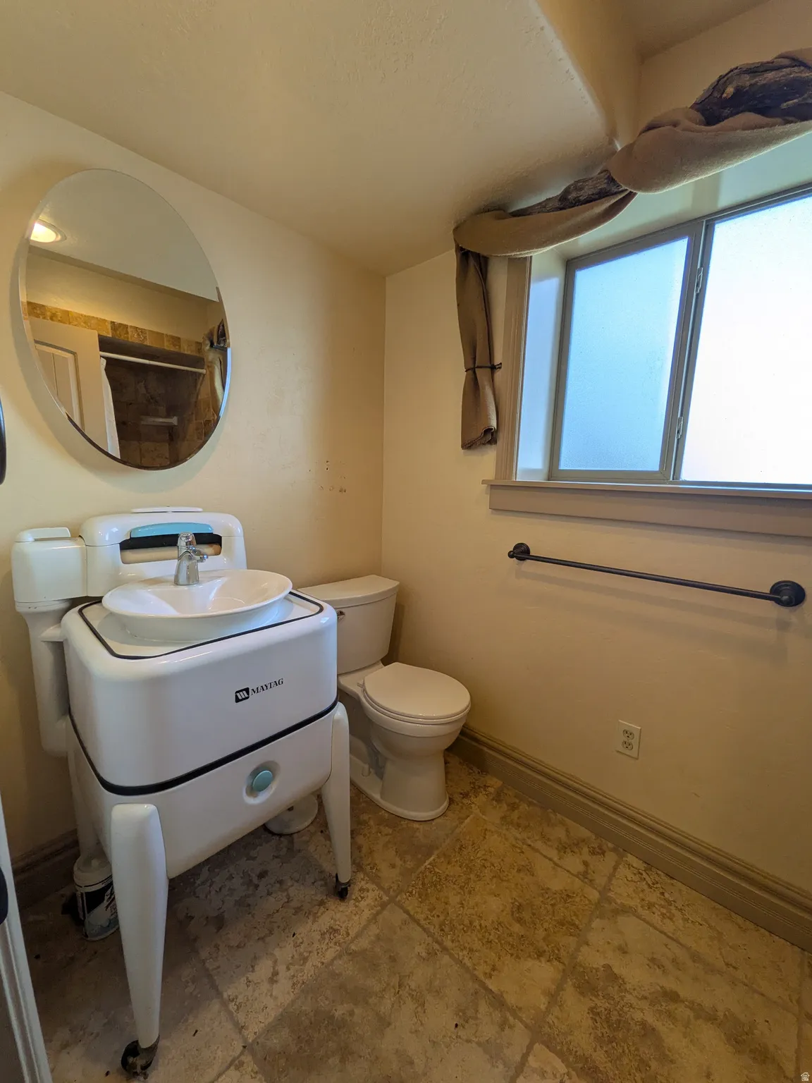 Ceramic tile flooring, white pedestal sink, toilet, towel bar, and window