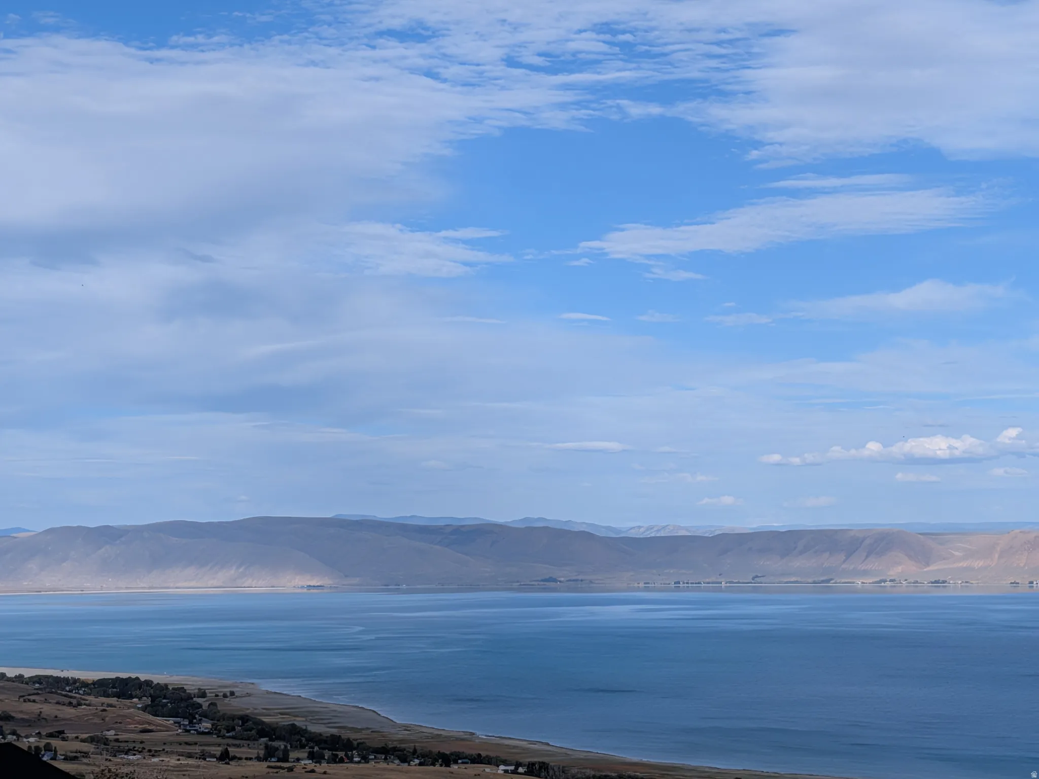 Expansive views of beautiful Bear Lake with a visible shoreline, complemented by distant mountains under a blue sky with scattered clouds