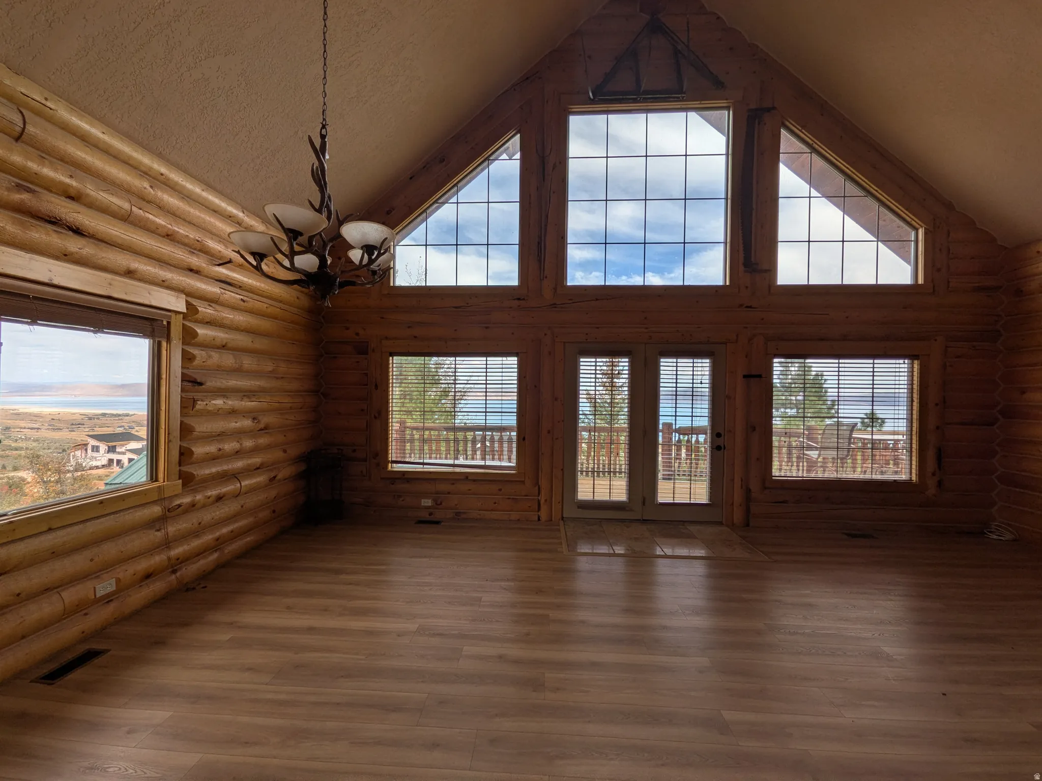 Vaulted ceiling, wood-finish flooring, log wall construction, antler-style chandelier, and large pane windows
