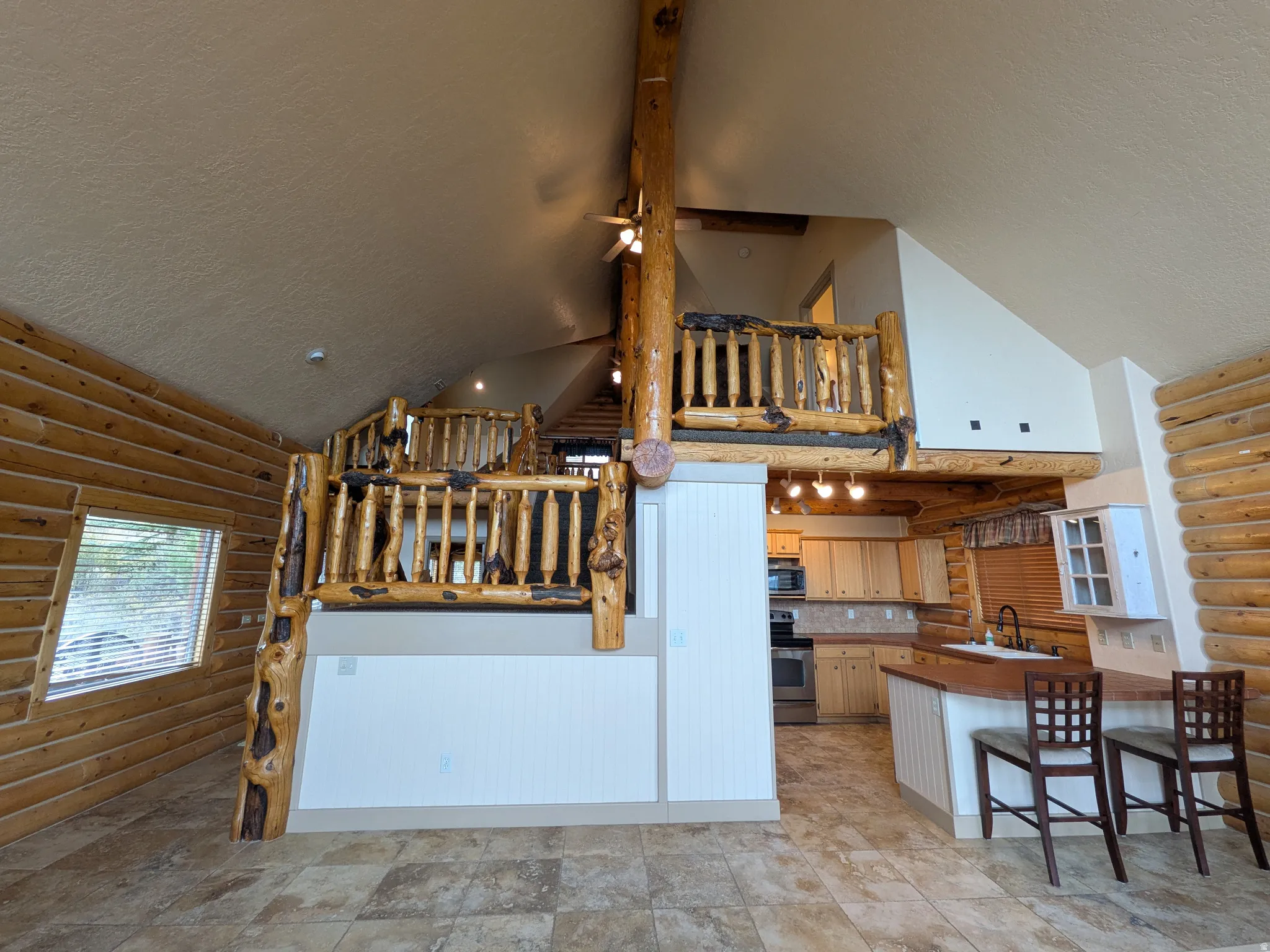 Loft space with log railing, tile flooring, full kitchen, and wood-paneled walls