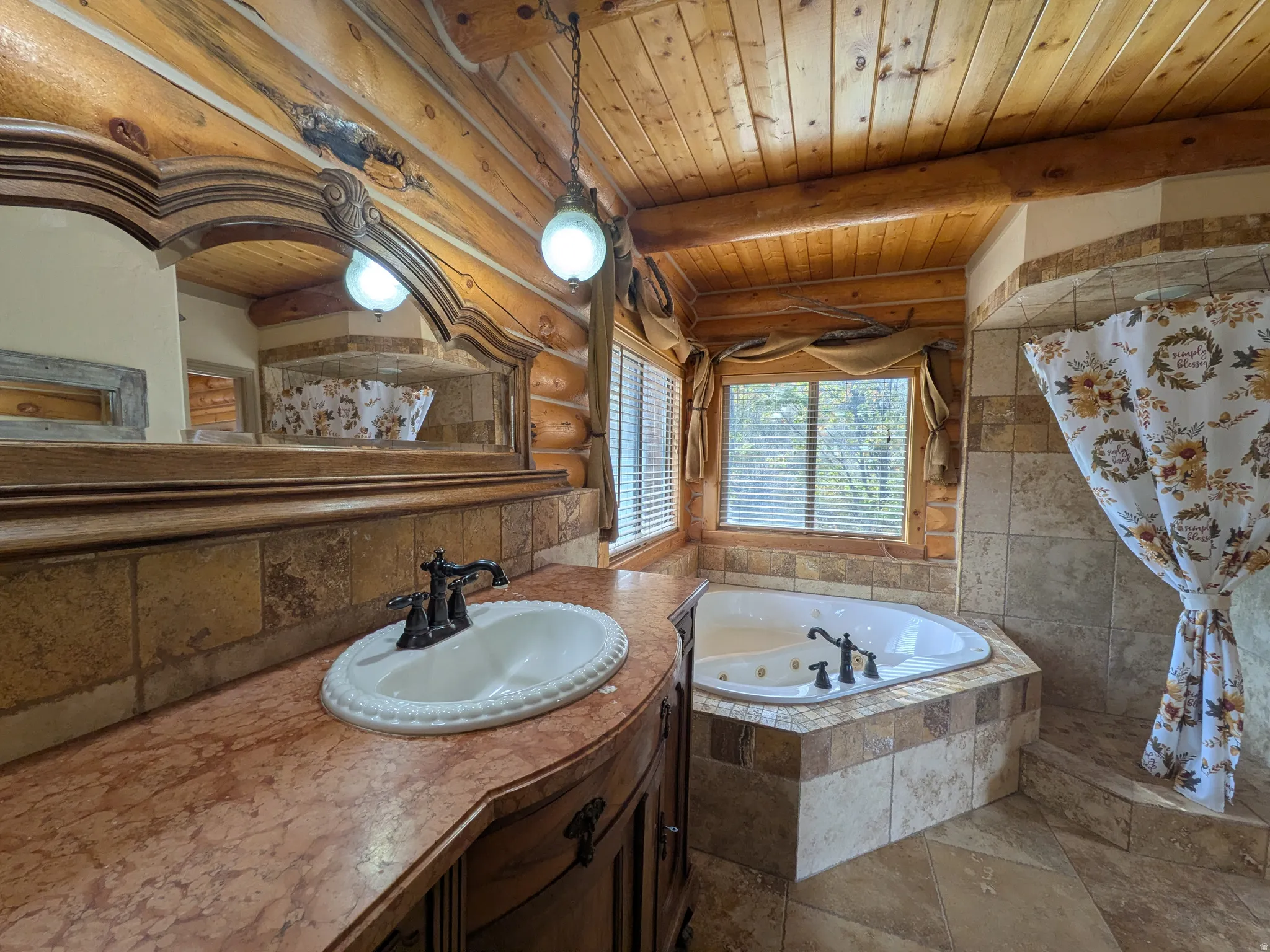 Wood-paneled walls and ceiling, corner jetted tub, tile surround, vanity with an integrated sink, and an ornate framed mirror