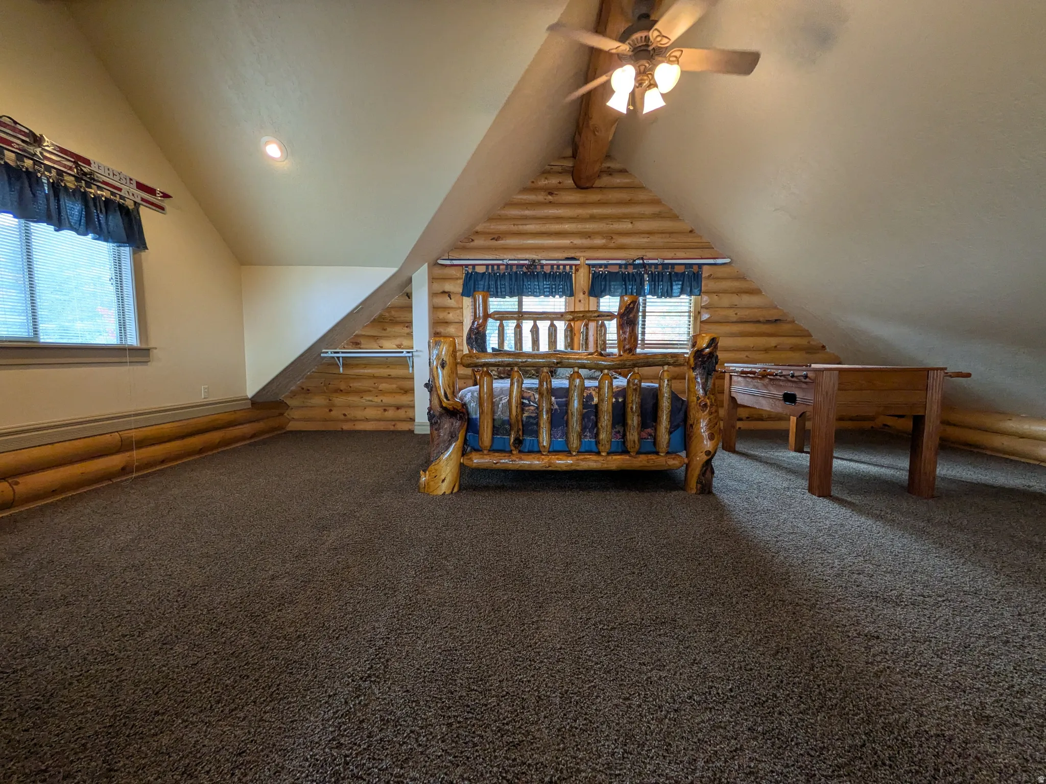 Carpeted room with a vaulted ceiling, exposed log beam, log wall detailing, and a ceiling fan with integrated lighting