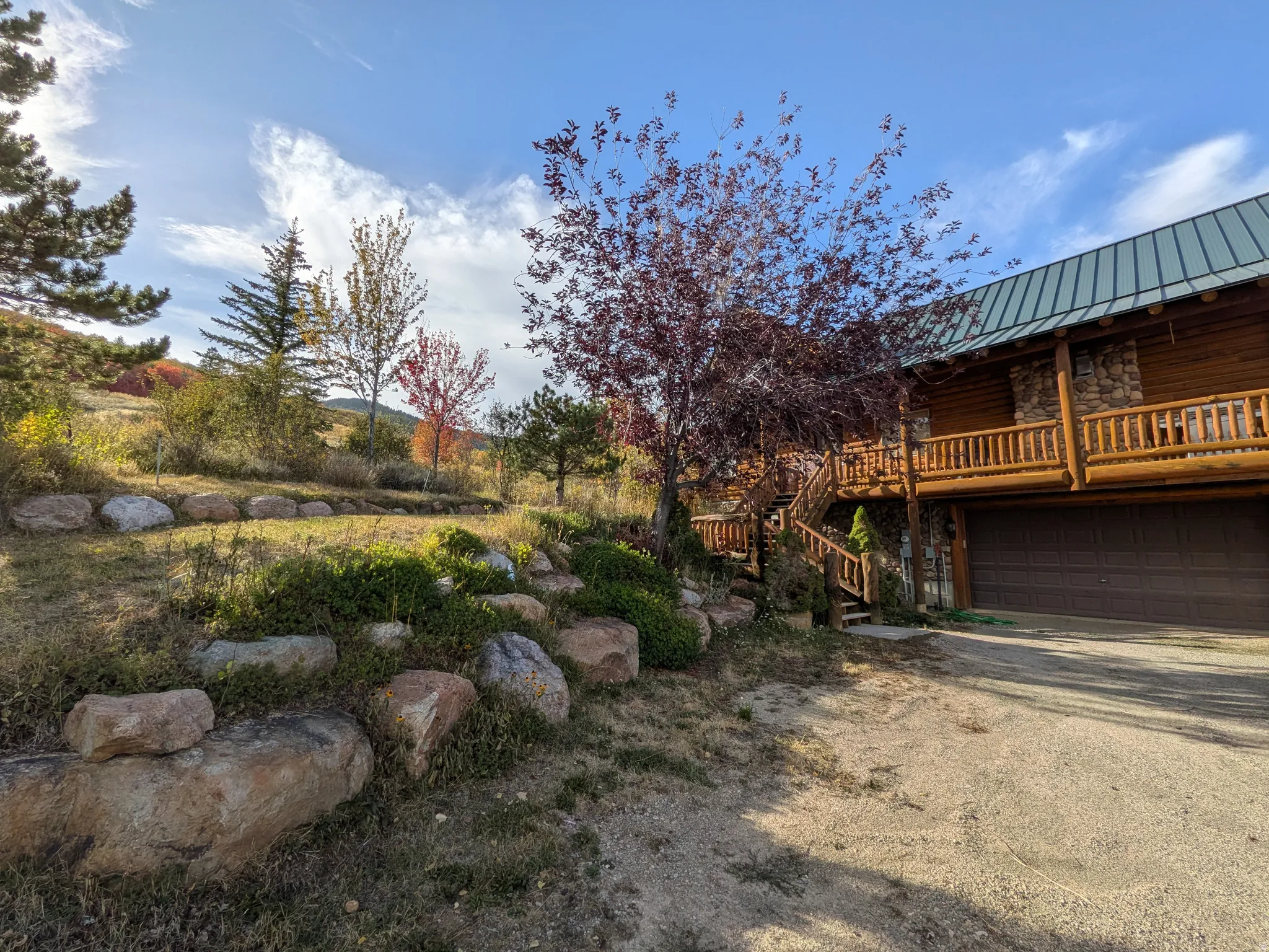 Log cabin exterior with an attached garage, a second-story balcony, and a green metal roof