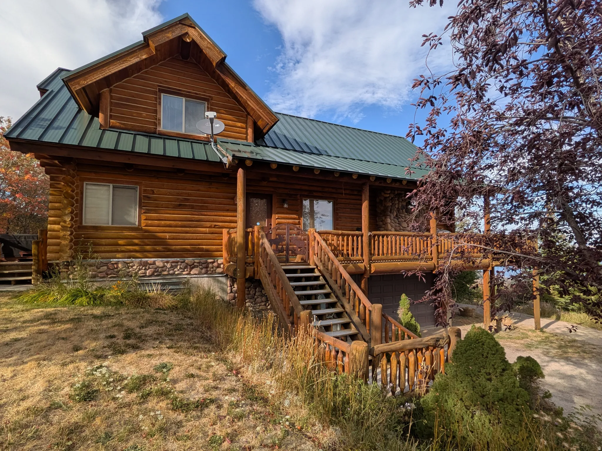 Log cabin exterior with a green metal roof, stone foundation, and a prominent wood deck