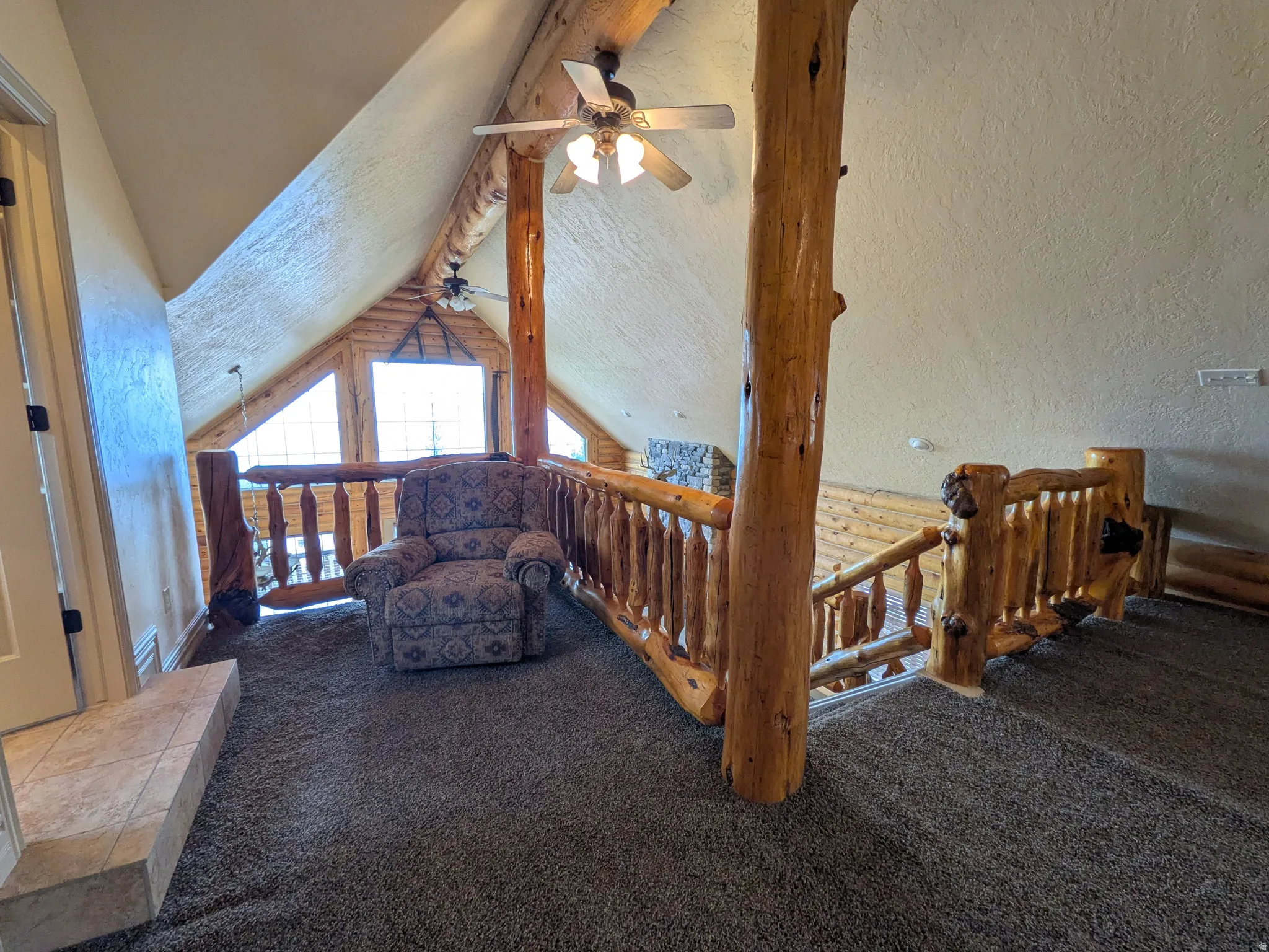 Vaulted ceiling featuring exposed log beams, rustic wood railing, and a ceiling fan