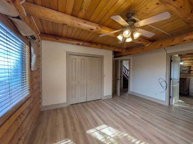 Wood-finish flooring with a ceiling fan light fixture, double bi-fold closet doors, and exposed wood beams