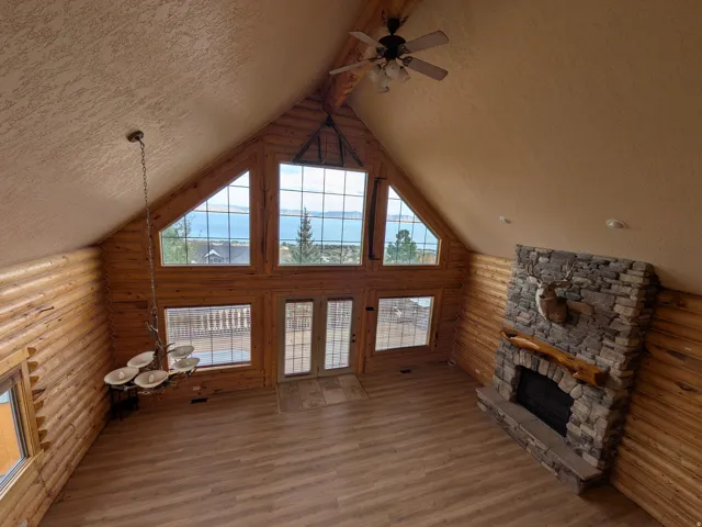 Vaulted ceiling with exposed wood-finish beams, large windows, stone fireplace, wood-finish flooring, and log wall construction