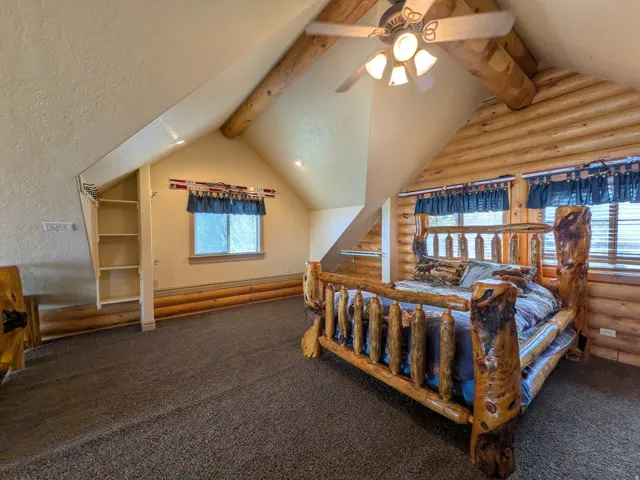 Sloped ceilings featuring wood beams, built-in shelving, carpet flooring, and log-style wall finishes