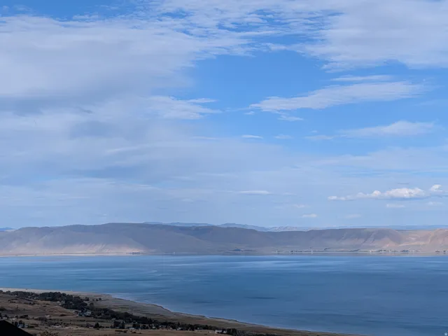Expansive views of beautiful Bear Lake with a visible shoreline, complemented by distant mountains under a blue sky with scattered clouds