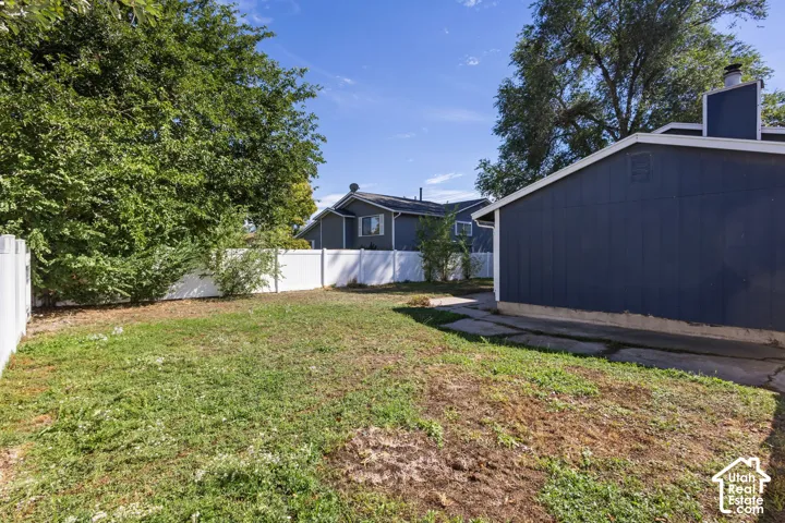 Expansive grassy yard with a white privacy fence and mature trees