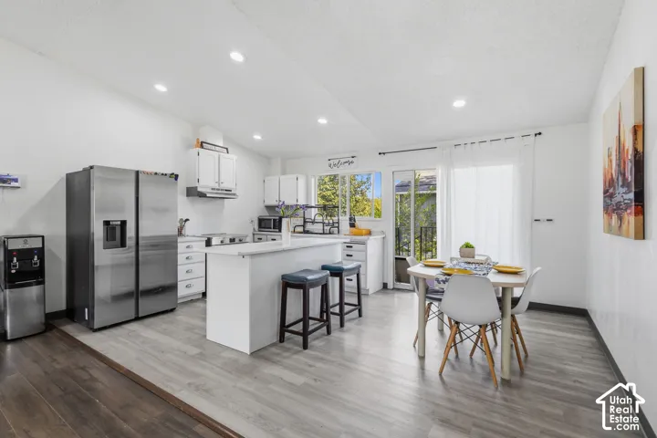 Modern kitchen featuring white cabinetry, stainless steel appliances, an eat-at island, and wood-finish flooring