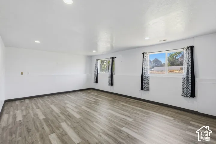 Spacious room featuring recessed lighting, two windows, and wood-finish flooring